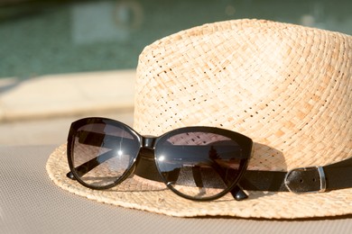 Stylish hat and sunglasses near outdoor swimming pool, closeup