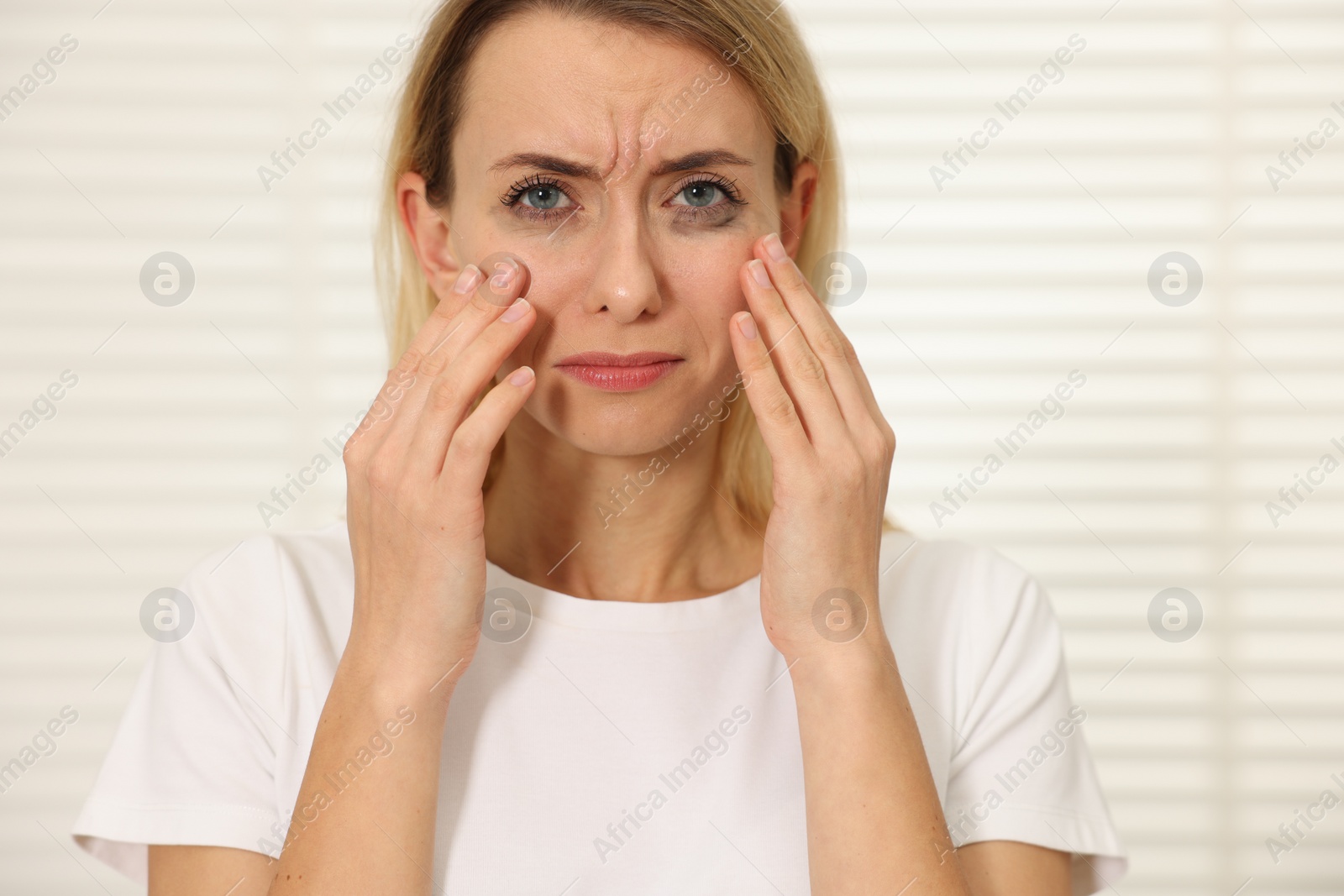 Photo of Sad woman with smeared mascara crying indoors