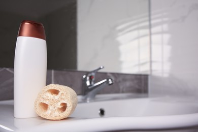 Natural loofah sponge and bottle of shower gel on washbasin in bathroom, space for text