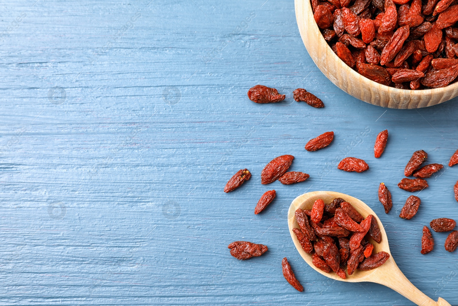 Photo of Dried goji berries on blue wooden table, flat lay. Space for text