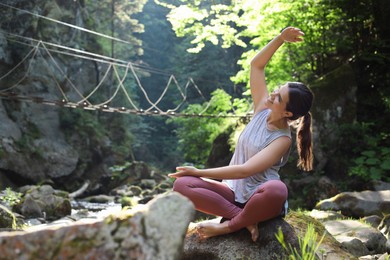 Happy young woman doing morning exercise in mountains