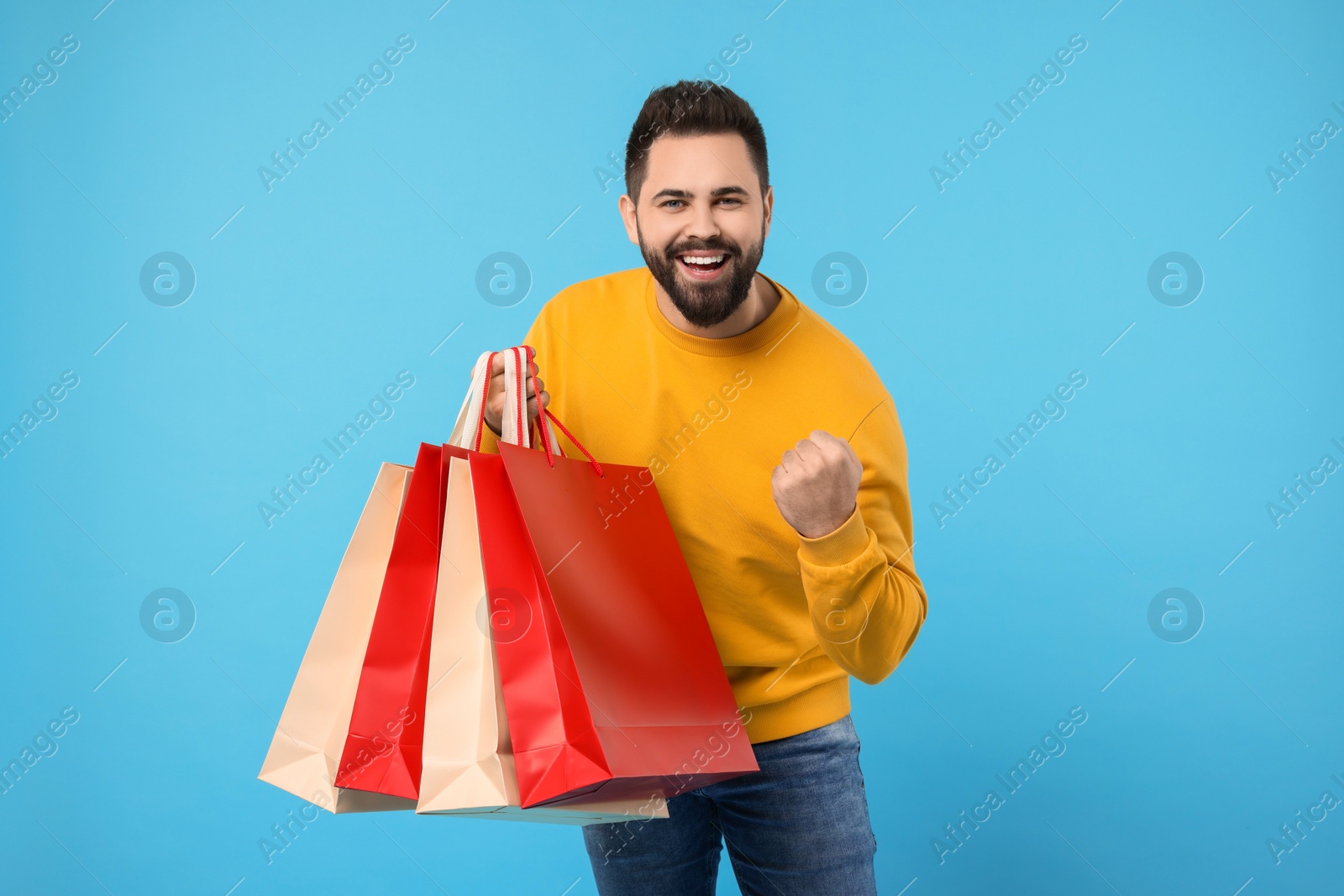 Photo of Excited man with many paper shopping bags on light blue background