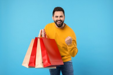 Excited man with many paper shopping bags on light blue background