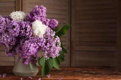 Photo of Beautiful lilac flowers in vase on wooden table. Space for text
