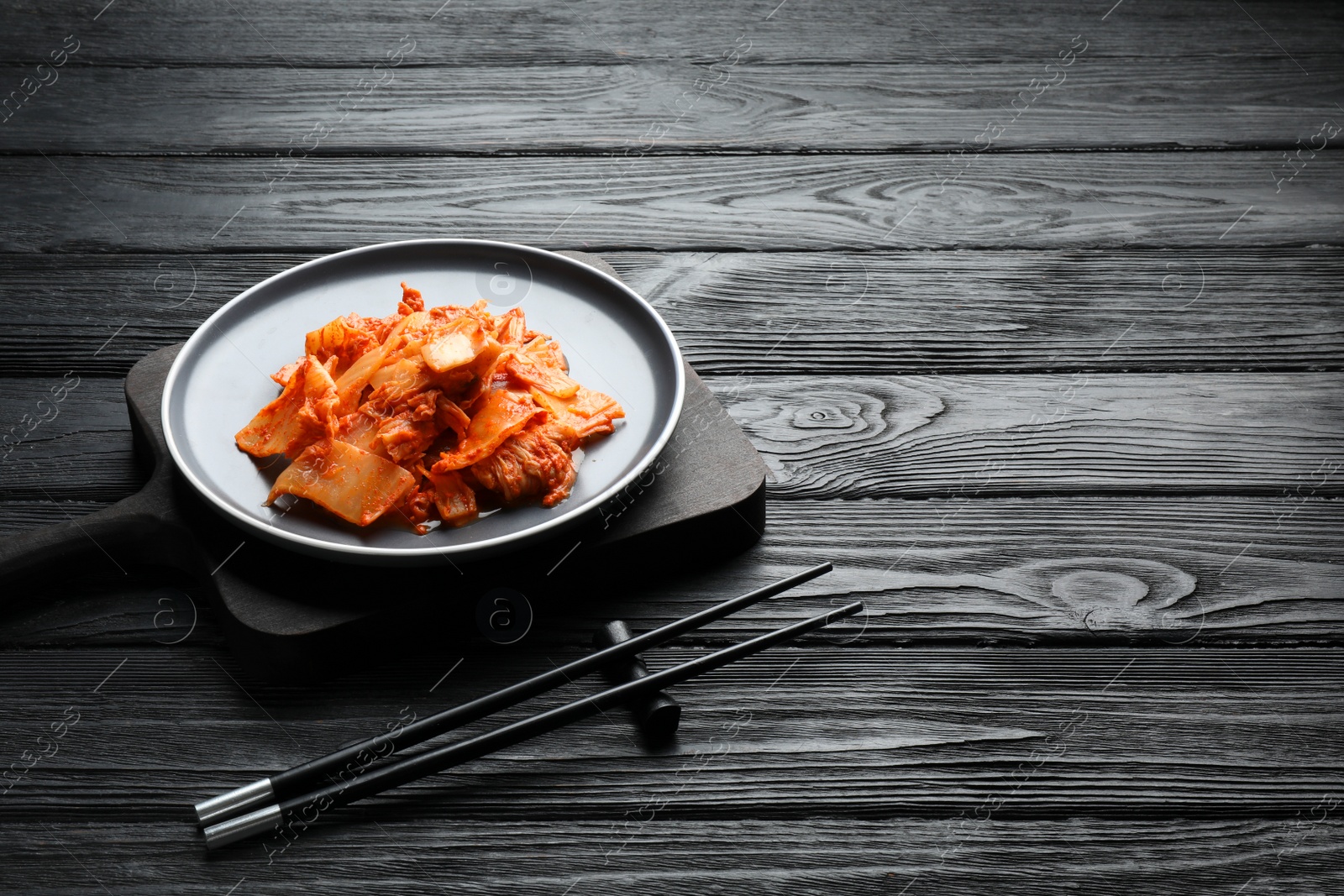 Photo of Delicious kimchi with Chinese cabbage served on black wooden table. Space for text