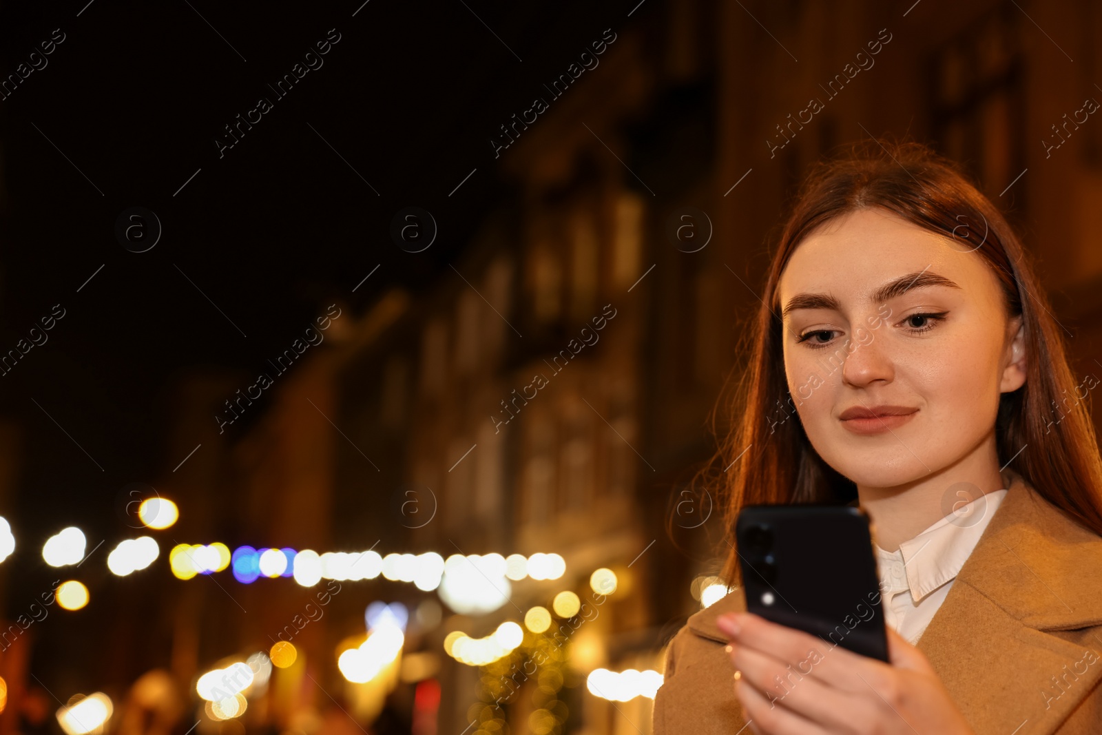 Photo of Beautiful woman using smartphone on night city street. Space for text