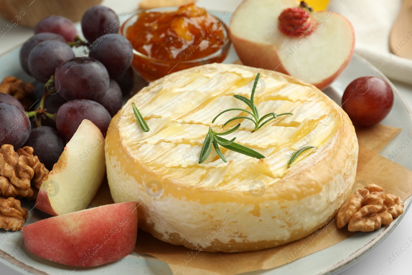 Photo of Tasty baked brie cheese with rosemary, fruits and walnuts on plate, closeup