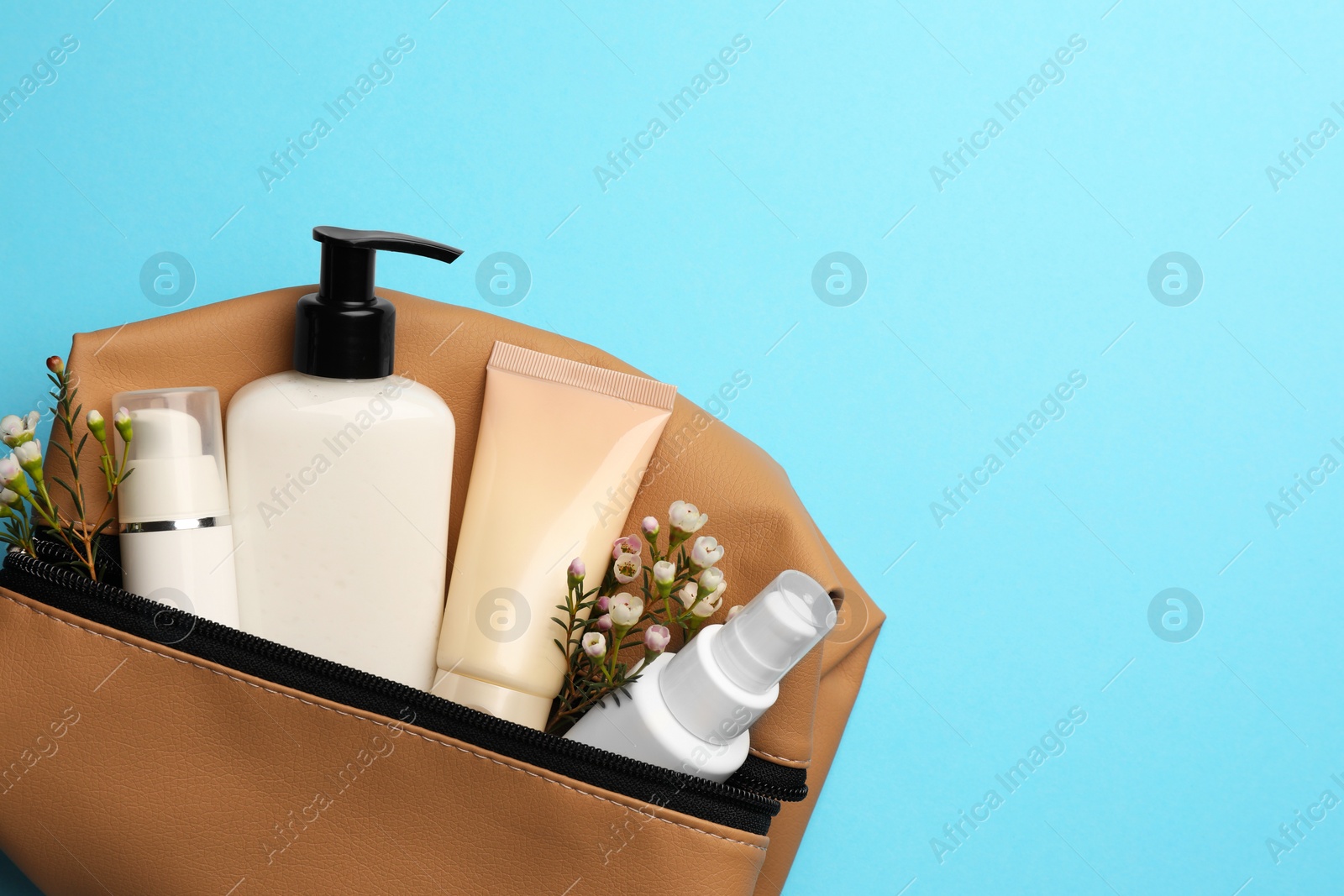 Photo of Preparation for spa. Compact toiletry bag with different cosmetic products and flowers on light blue background, top view. Space for text