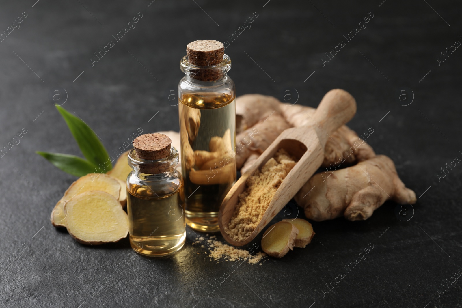 Photo of Glass bottles of essential oil, ginger powder and root on dark table