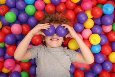 Happy little boy lying on many colorful balls, top view