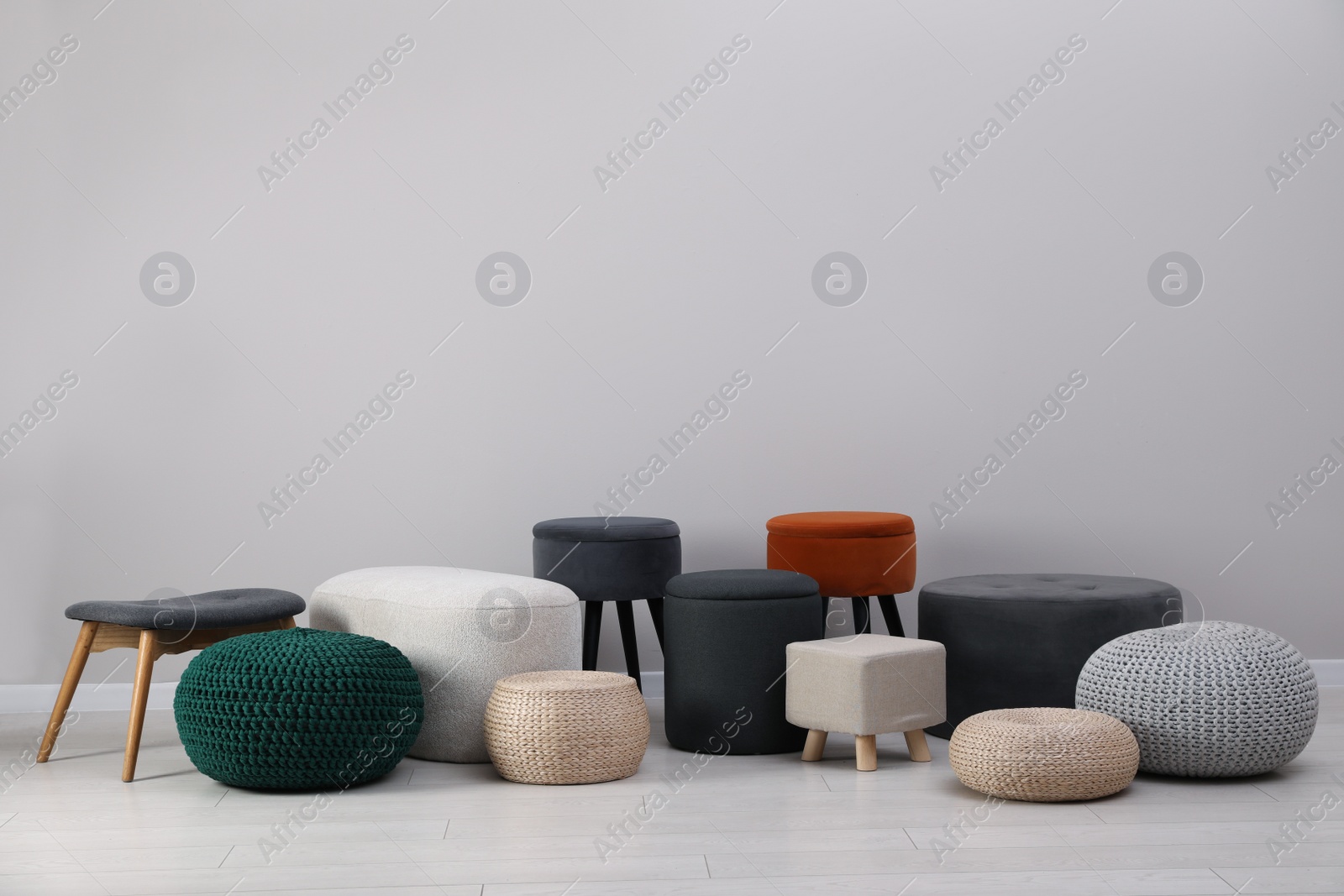 Photo of Different stylish poufs and ottomans near light grey wall