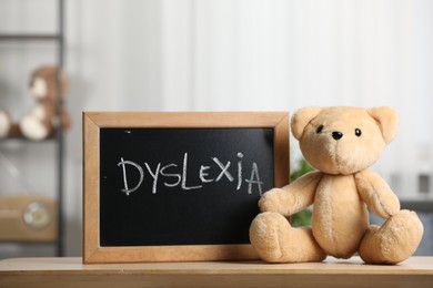 Photo of Teddy bear and small blackboard with word Dyslexia on wooden table in room