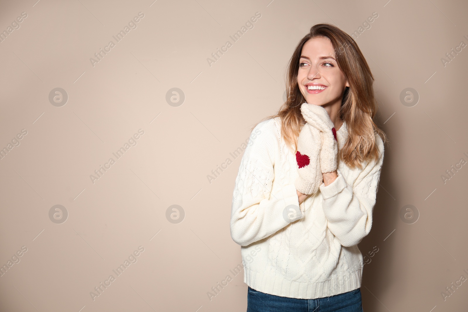 Image of Happy young woman wearing warm sweater and knitted mittens on beige background. Space for text