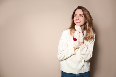 Happy young woman wearing warm sweater and knitted mittens on beige background. Space for text