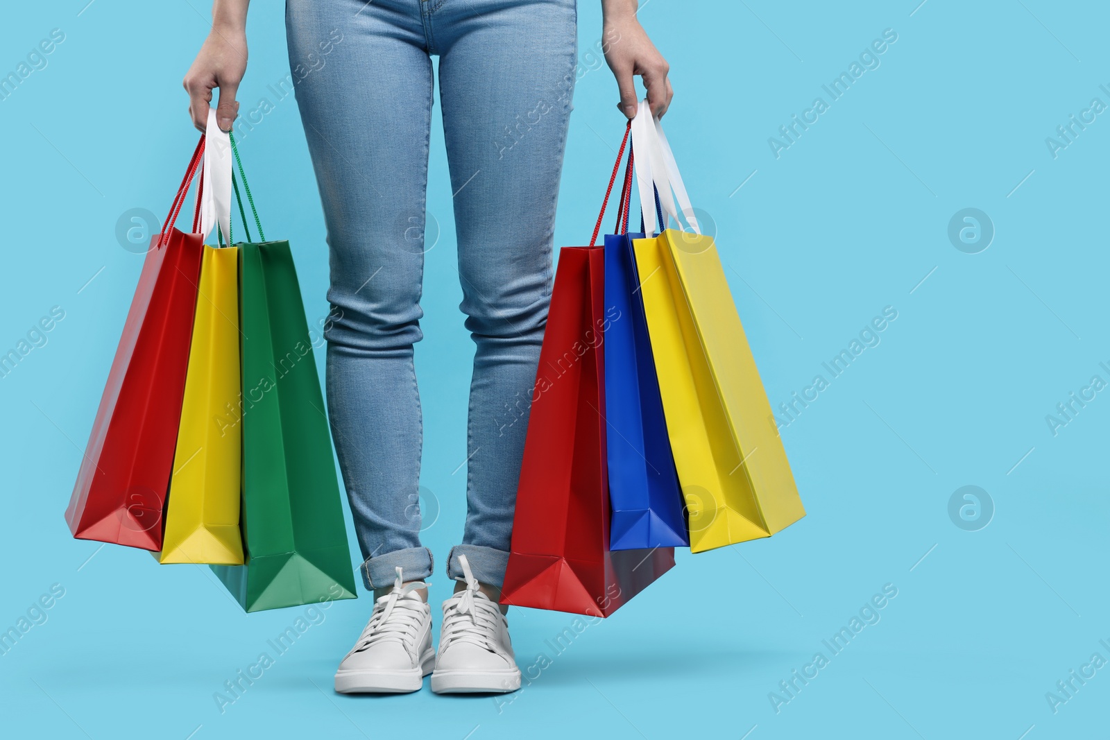 Photo of Woman with shopping bags on light blue background, closeup. Space for text