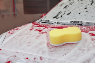 Photo of Auto covered with foam with sponge on hood at car wash, closeup
