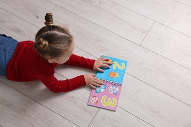 Photo of Cute little girl reading book on warm floor indoors, space for text. Heating system