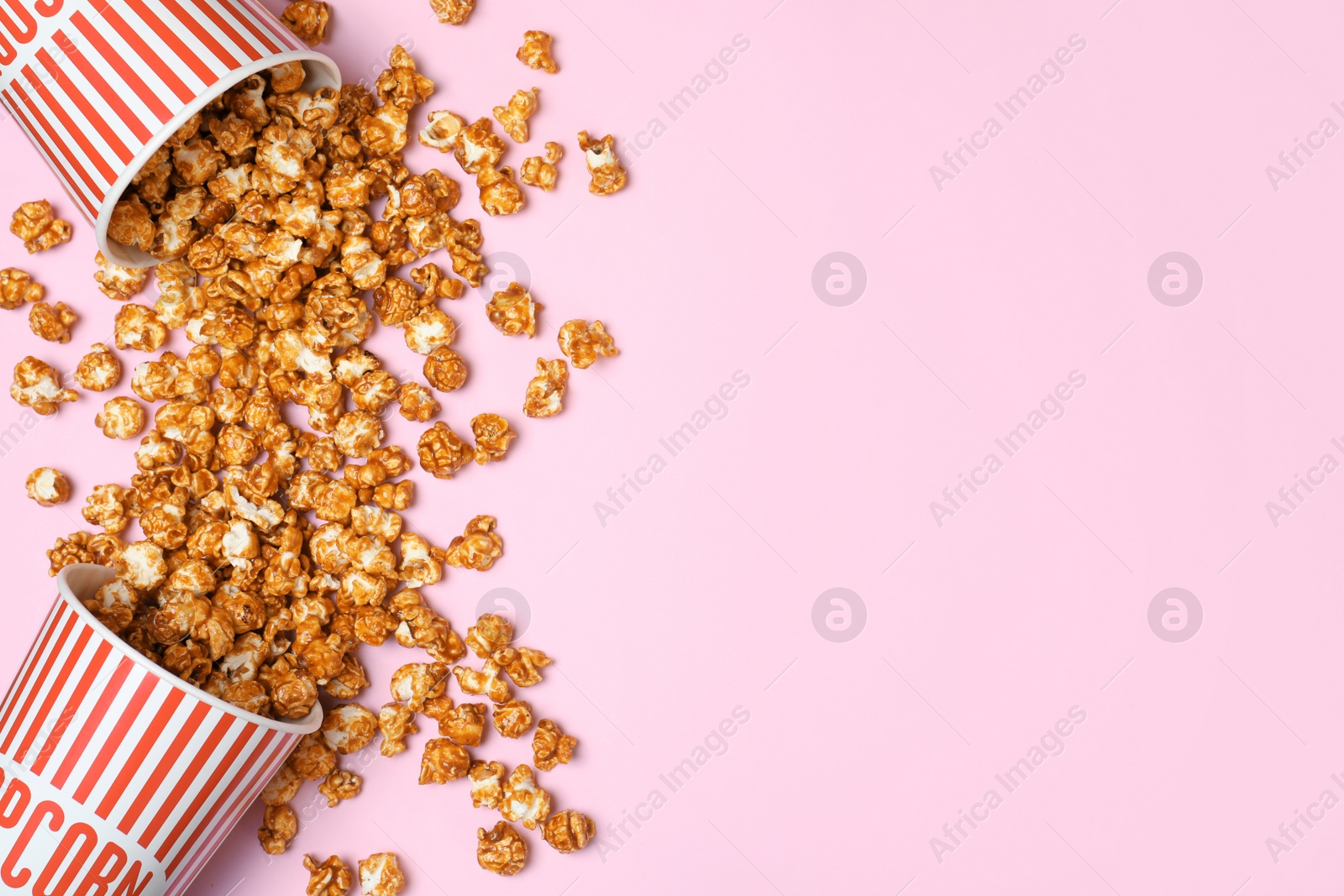 Photo of Overturned paper cups with caramel popcorn on color background, top view. Space for text