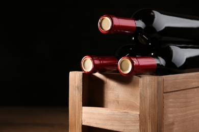 Photo of Wooden crate with bottles of wine on dark background, closeup