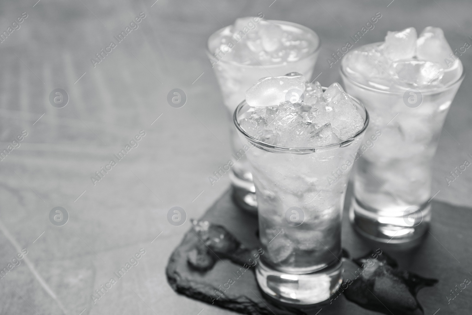 Photo of Shot glasses with vodka and ice on grey table. Space for text