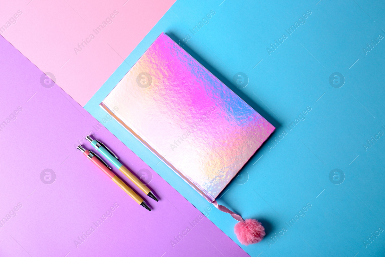 Photo of Shiny notebook with pink pompom and pens on color background, flat lay