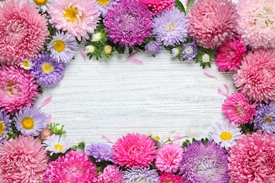 Photo of Frame made of beautiful aster flowers on white wooden table. Space for text