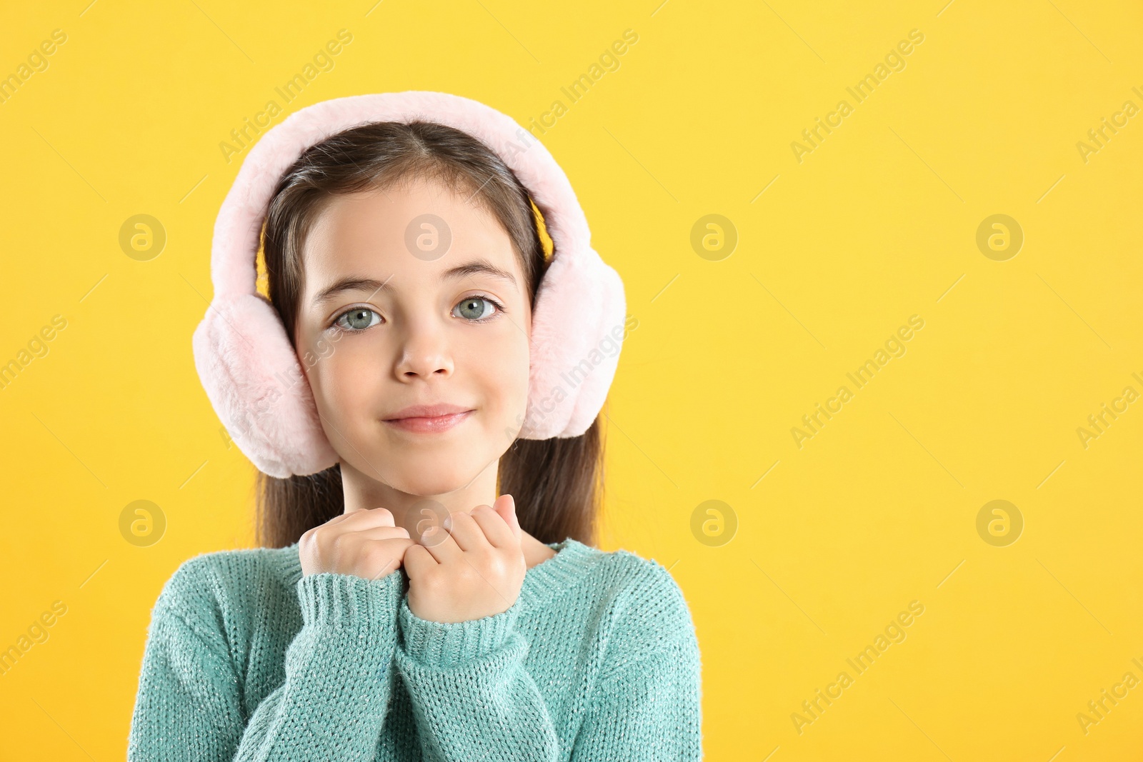 Photo of Cute girl wearing stylish earmuffs on yellow background. Space for text