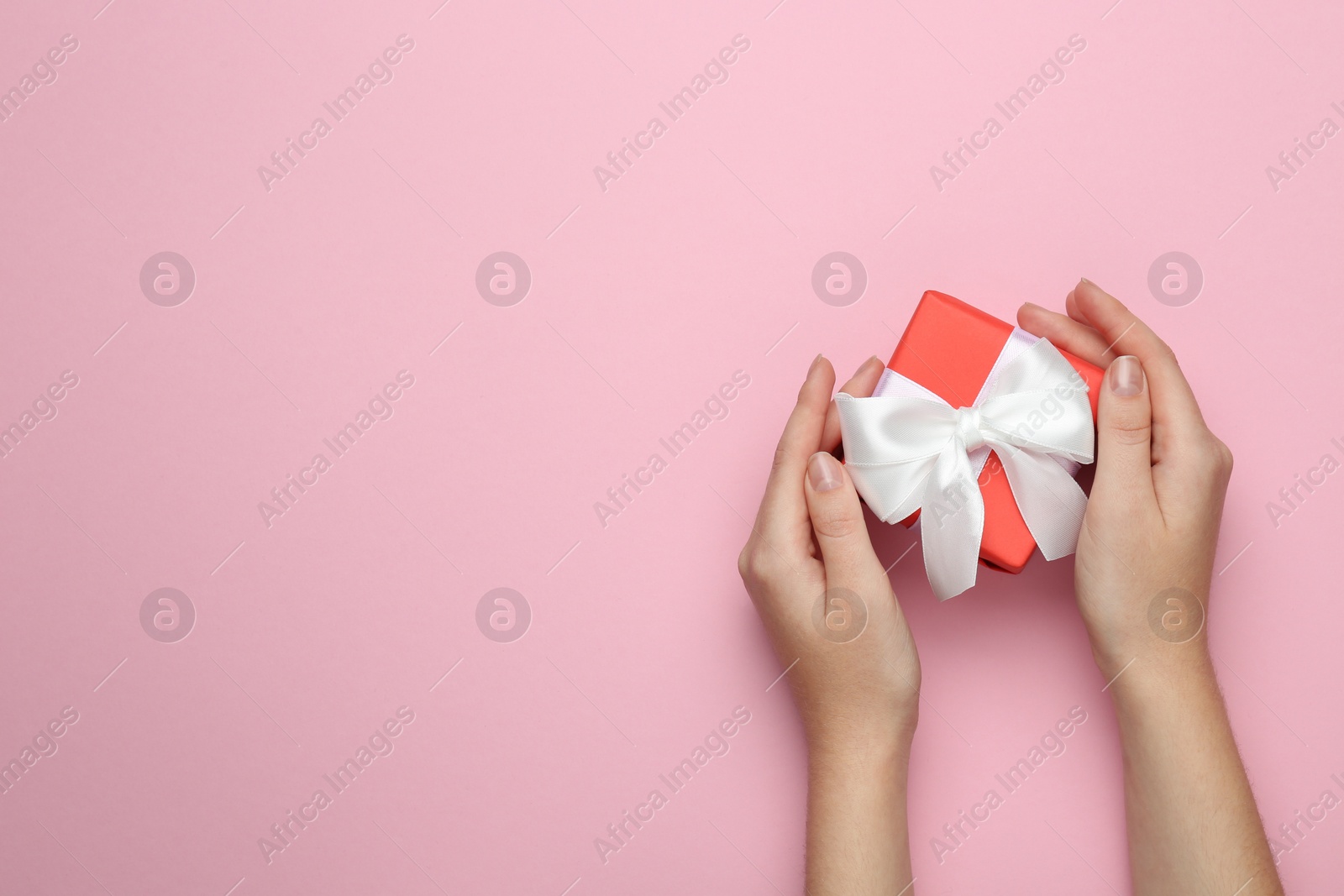 Photo of Woman holding beautiful gift box on pink background, top view. Space for text