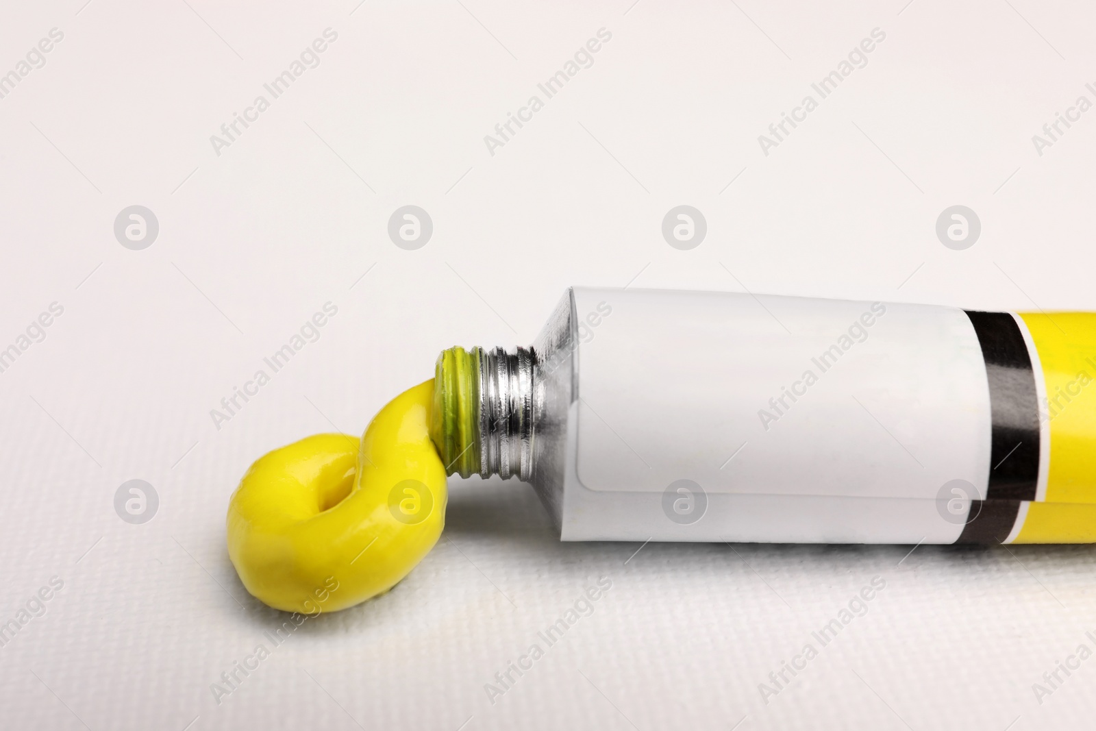 Photo of Tube with yellow oil paint on blank canvas, closeup