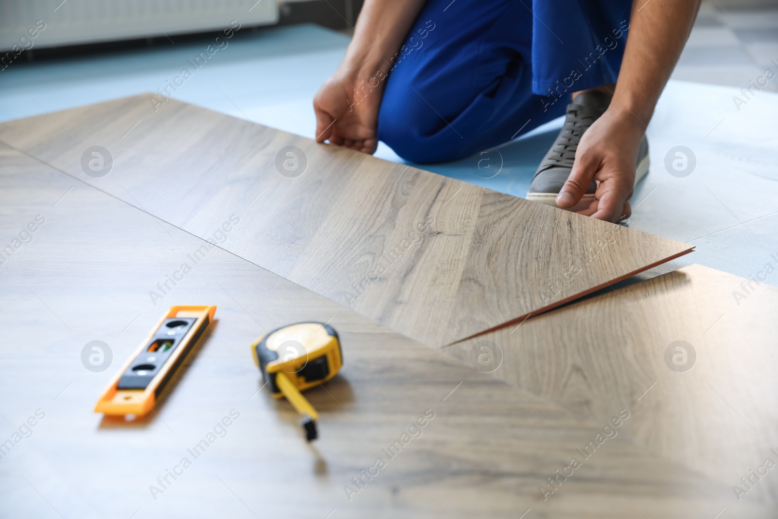 Photo of Worker installing laminated wooden floor indoors, closeup