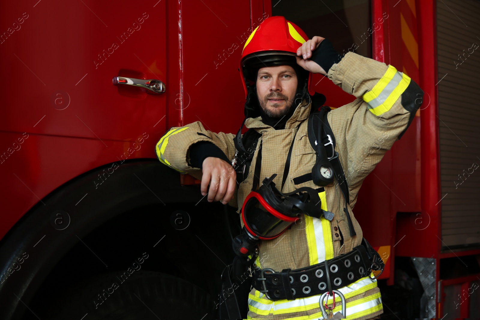 Photo of Portrait of firefighter in uniform near red fire truck at station