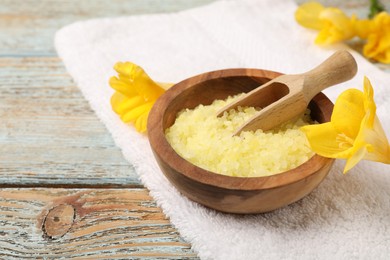 Photo of Yellow sea salt in bowl, scoop, flowers and towel on wooden table, space for text