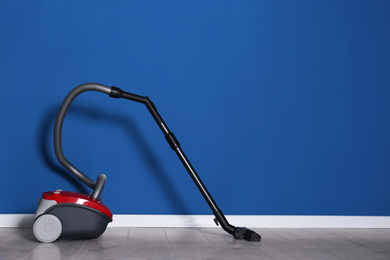 Modern red vacuum cleaner on floor near blue wall, space for text