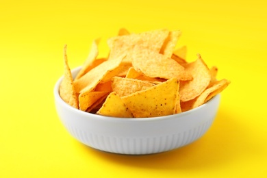 Photo of Tasty mexican nachos chips in bowl on yellow background