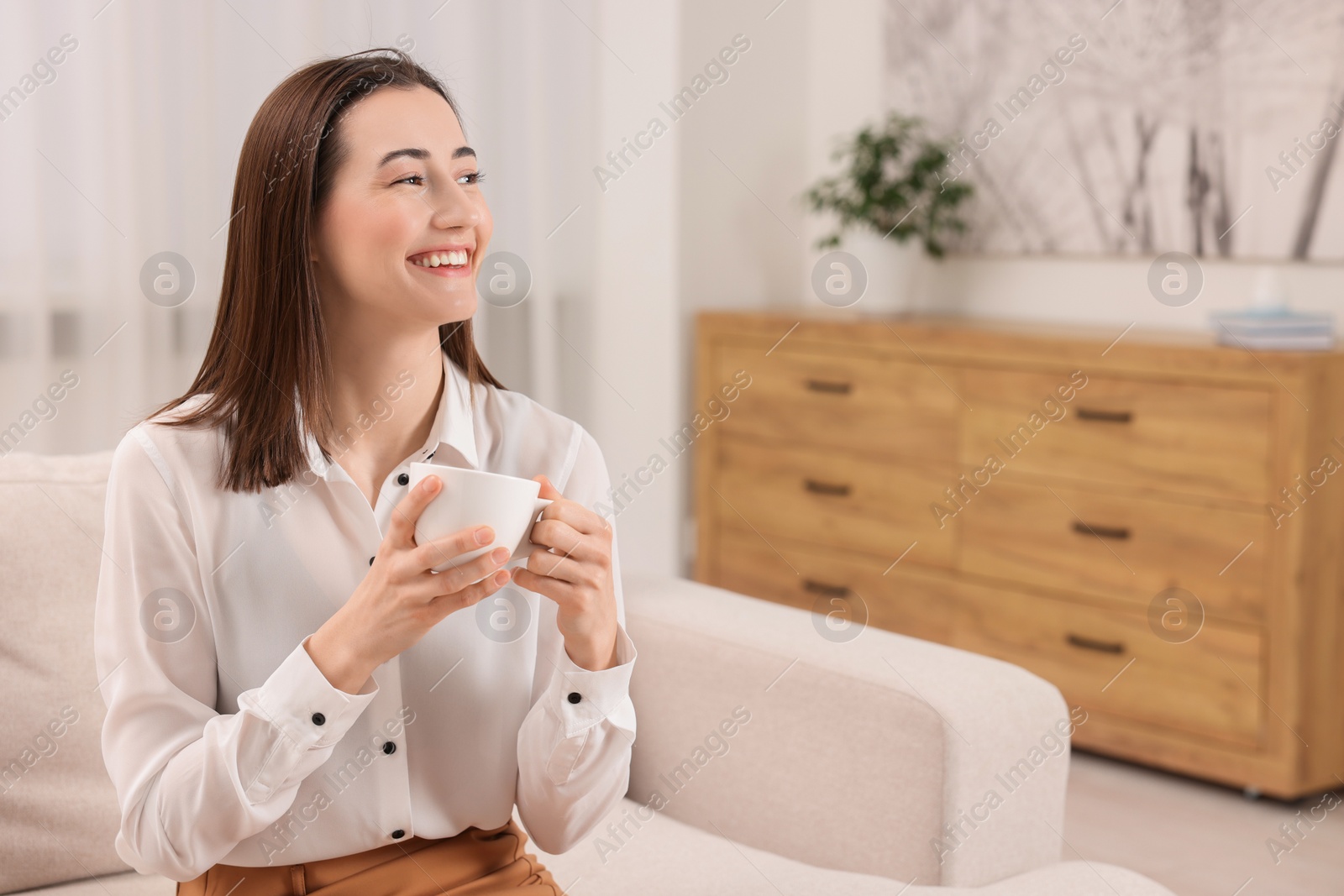 Photo of Beautiful woman with cup of coffee smiling in room, space for text