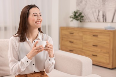 Photo of Beautiful woman with cup of coffee smiling in room, space for text