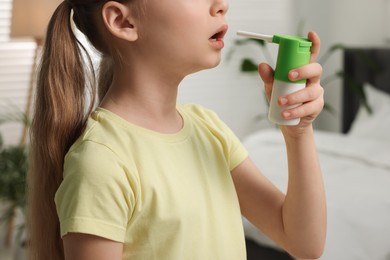 Photo of Little girl using throat spray at home, closeup