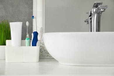 Electric toothbrushes and tube of paste near vessel sink on countertop in bathroom, closeup