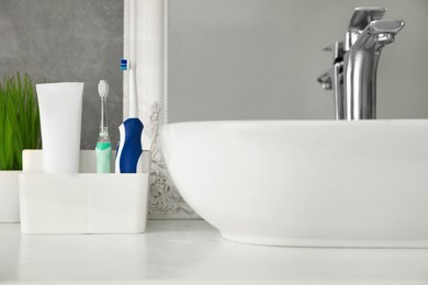 Photo of Electric toothbrushes and tube of paste near vessel sink on countertop in bathroom, closeup