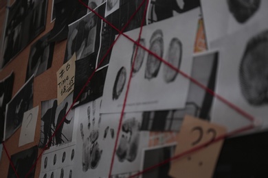 Photo of Detective board with crime scene photos, stickers, clues and red thread, closeup