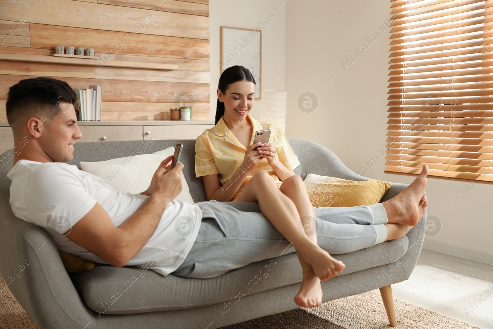 Photo of Happy couple in pyjamas with gadgets spending time together on sofa at home