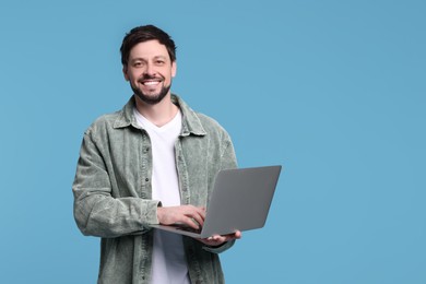 Happy man with laptop on light blue background, space for text