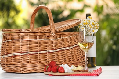 Photo of Picnic basket and wine with products on table against blurred background