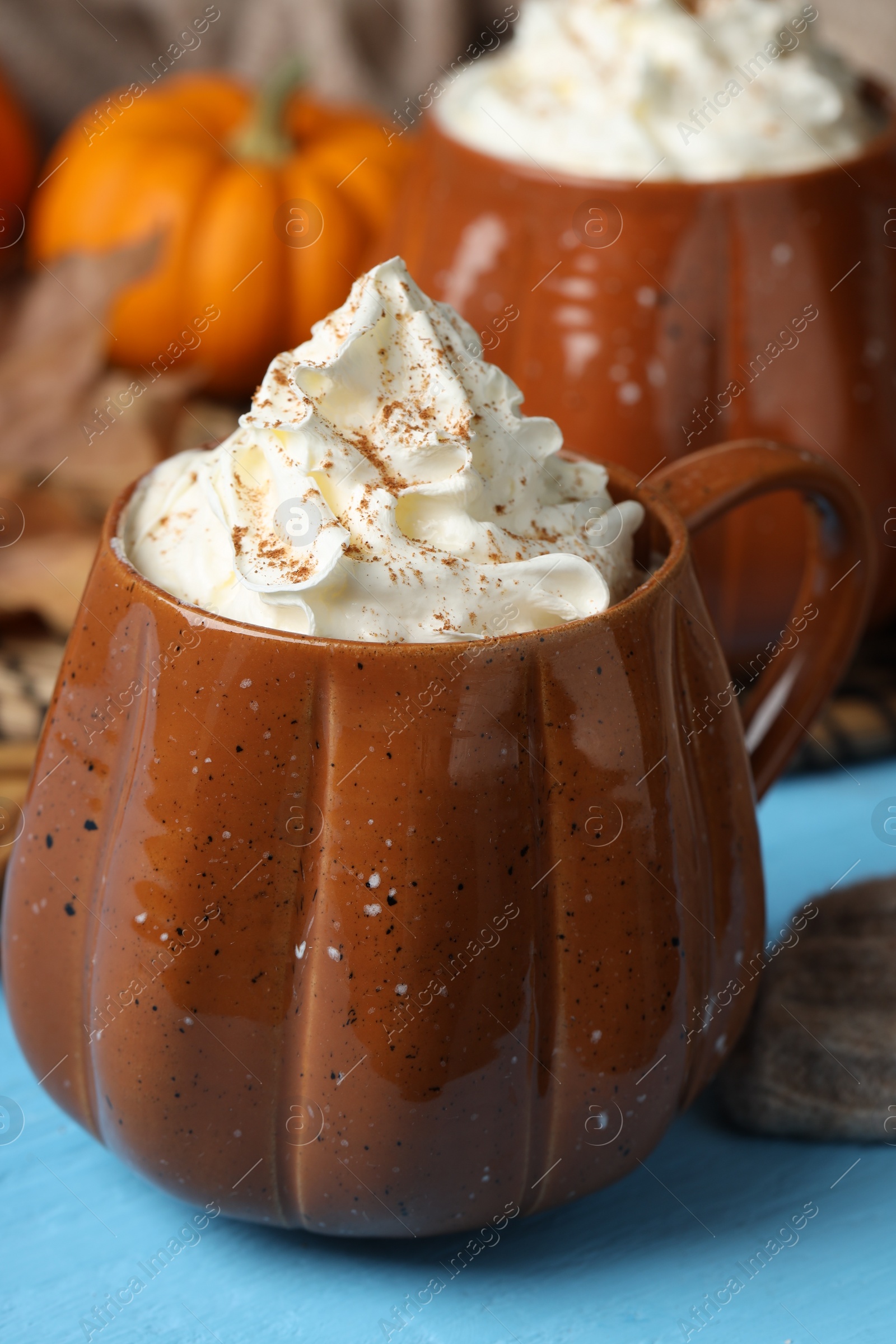 Photo of Mugs of pumpkin spice latte with whipped cream on light blue wooden table, closeup