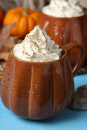 Mugs of pumpkin spice latte with whipped cream on light blue wooden table, closeup