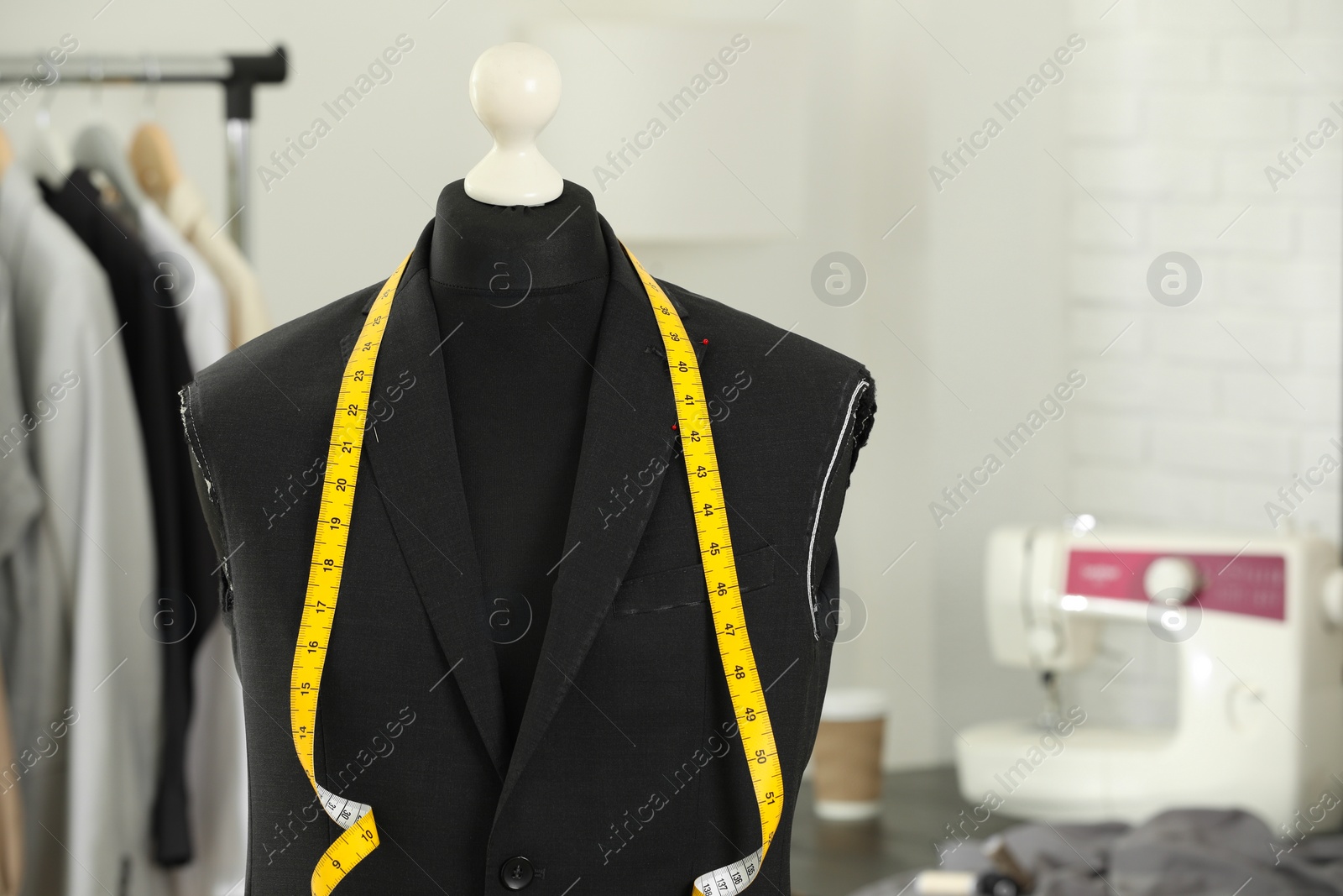 Photo of Mannequin with unfinished jacket and measuring tape in tailor shop, closeup. Space for text