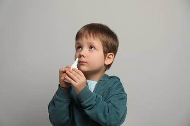 Photo of Little boy using nasal spray on light grey background