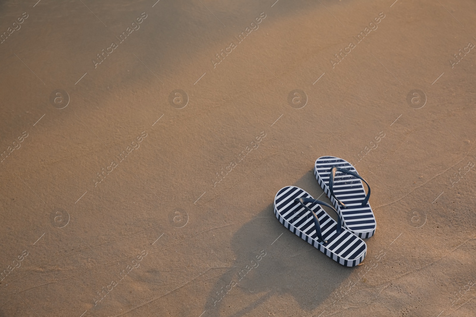 Photo of Striped beach slippers on sand, space for text