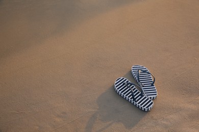 Photo of Striped beach slippers on sand, space for text