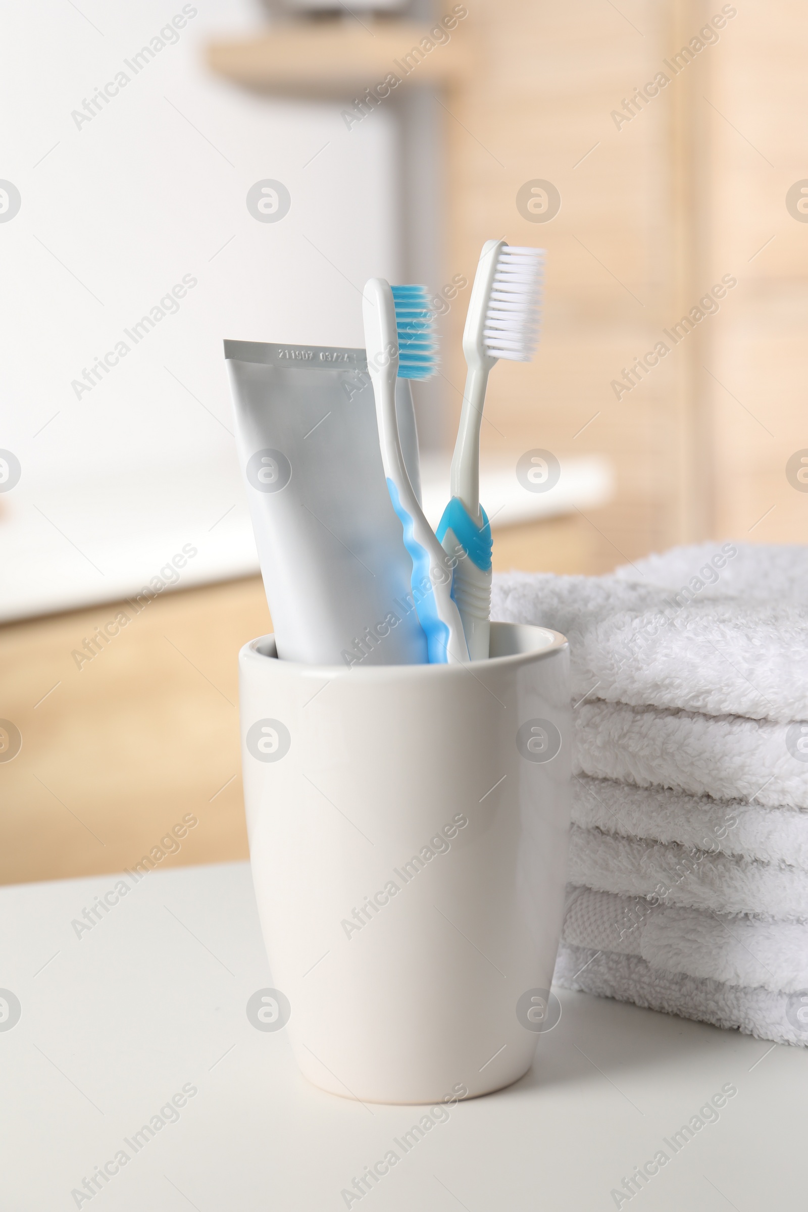Photo of Plastic toothbrushes, toothpaste and towels on white countertop in bathroom